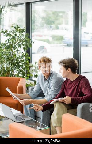 Zwei männliche Studenten sitzen auf einer Couch in einem Büro, diskutieren Ideen und denken zusammen. Stockfoto