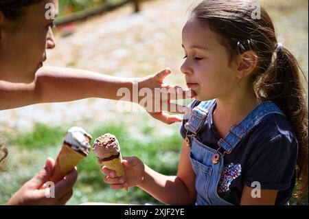 Eine liebevolle Mutter und ihre Tochter verbringen einen zärtlichen Moment, während sie Eiskegel in einem sonnigen Park essen. Warme und fröhliche Outdoor-Szene. Stockfoto