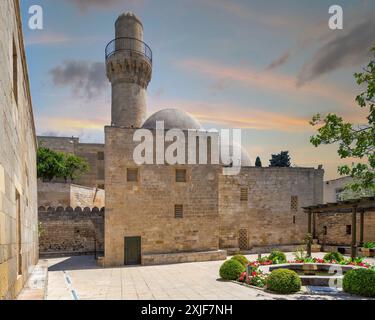 Der Sonnenuntergang des Minaretts der Schah-Moschee erhebt sich über den umliegenden Gebäuden in Baku, Aserbaidschan. Diese Moschee ist neben dem Palast der Shirvanshahs ein prominentes Wahrzeichen der Stadt Stockfoto