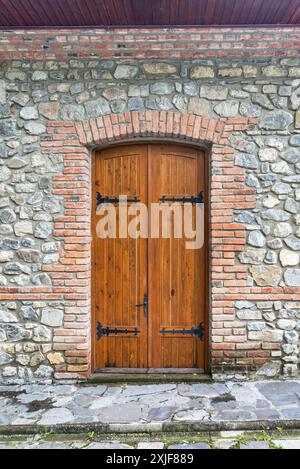 Eine Reihe von Doppeltüren aus Holz mit schwarzen Eisenscharnieren befindet sich in einer bogenförmigen Öffnung einer Steinmauer Stockfoto