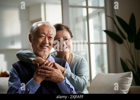 Porträt eines glücklichen liebenden asiatischen Seniorenpaares, das zu Hause auf der Couch sitzt Stockfoto