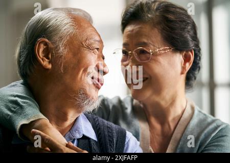 Porträt eines glücklichen liebenden asiatischen Seniorenpaares, das zu Hause auf der Couch sitzt Stockfoto