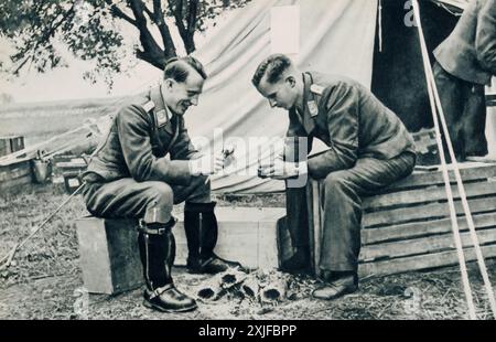 Ein Foto zeigt deutsche Soldaten in einem temporären Lager, die vor ihrem Zelt sitzen und Kartoffelpuffer zubereiten. Diese Szene bietet einen Einblick in ihr tägliches Leben während der Operation Barbarossa im Jahr 1941, als sie in Richtung Ostfront vorrückten. Stockfoto