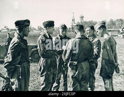 Ein Foto zeigt eine Gruppe von Soldaten, die ihre letzte Mission diskutieren, nachdem sie von einem Kampfflug zurückgekehrt sind. Sie erzählen von ihrer Begegnung mit sowjetischen Kämpfern und wie sie es geschafft haben, sie abzuwehren. Diese Szene wurde 1941 während der Operation Barbarossa aufgenommen und zeigt die Kameradschaft und die gemeinsamen Erfahrungen der deutschen Streitkräfte, die während des Zweiten Weltkriegs gegen sowjetische Truppen an der Ostfront vorrückten. Stockfoto
