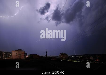 Donner über Vororte. Ein Blitz am purpurpurnen Himmel beleuchtet wenige Wolken. Stockfoto