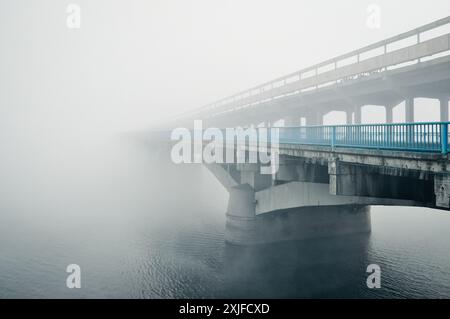 Brücke ins Nirgendwo. Betonbrücke über einen Fluss, der von dickem Nebel bedeckt ist. Perspektivische Ansicht einer Brücke, die in dichtem Nebel verschwindet. Stockfoto