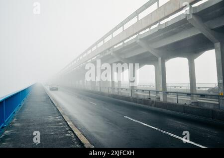 Autos fahren auf einer Brücke ins Nirgendwo. Betonbrücke mit dickem Nebel bedeckt. Perspektivische Ansicht einer Brücke, die in dichtem Nebel verschwindet. Schlechte Sicht. Stockfoto