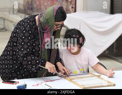 Teheran, Iran. Juli 2024. Ein Kind versucht, Teppichherstellung in einem Teppichmuseum in Teheran, Iran, 18. Juli 2024. Quelle: Shadati/Xinhua/Alamy Live News Stockfoto