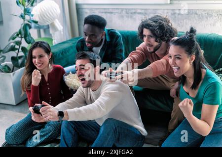 Fröhliche Gruppe von Freunden, die zu Hause gemeinsam Videospiele spielen, Freizeit- und Unterhaltungskonzept Stockfoto