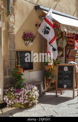 ALGHERO, ITALIEN - 4. JULI 2024: Mittelalterliche malerische Straße typisch sardisch mit kleinen traditionellen Restaurants und Souvenirladen. Die Flagge des Profis Stockfoto