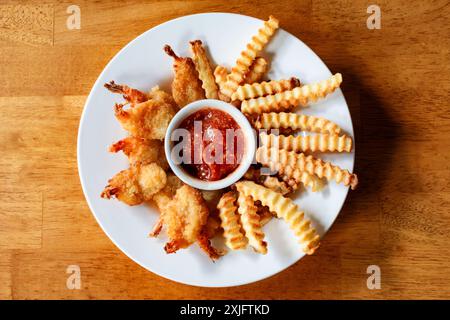 Frittierte Garnelen und Pommes frites, die in einer Luftfritteuse gekocht werden. In einer flachen weißen Schüssel mit Cocktailsauce in der Mitte angeordnet. Stockfoto