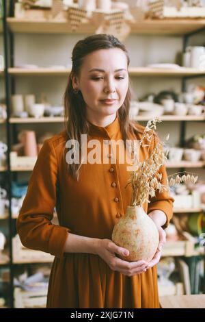 Elegante Handwerkerin und dekorative Keramik in Werkstatt. Nahaufnahme Porträt stilvolle Handwerker-Frau mit Ton-Vase. Töpferkunst. Handgefertigte Be Stockfoto