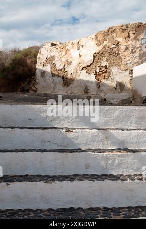 Treppe weiß von der Seite und schwarze Steinstruktur oben. Alter verwitterter Zaun mit abgespaltener Fassade im Hintergrund. Intensive weiße Wolken auf Stockfoto