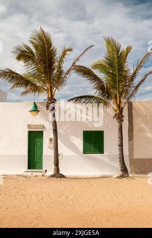 Sandstraße an der Küste des Atlantiks. Haus mit weißer Fassade. Palmen wachsen vor der Tür. Blauer Himmel mit weißen Wolken im Winter. Caleta Stockfoto