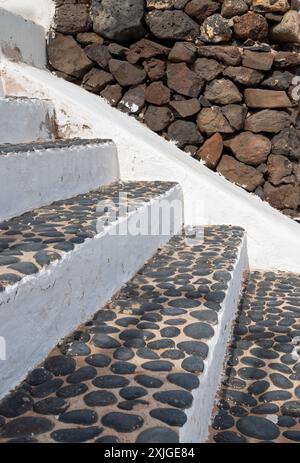Treppe weiß von der Seite und schwarze Steinstruktur oben. Alter verwitterter Zaun mit abgespaltener Fassade im Hintergrund. Intensive weiße Wolken auf Stockfoto