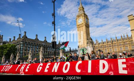 London, 18. Juli 2024. Vor dem Eingang des Parlaments wurde ein riesiges Plakat mit der Aufschrift „Stop the Genocide“ angebracht. Tausende pro-palästinensischer Aktivisten bilden heute Abend eine Menschenkette um das Parlament in Westminster und fordern von der neuen Regierung, den Waffenverkauf an die israelische Regierung einzustellen. Mehrere Abgeordnete schließen sich dem Protest an, während gegenüber auf dem Parlamentsplatz erneut eine israelische Gruppe gegen die Hamas und die Freilassung palästinensischer Geiseln protestiert. Quelle: Imageplotter/Alamy Live News Stockfoto