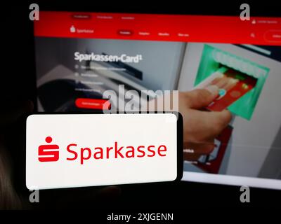 Person mit Smartphone und Logo des deutschen Finanzdienstleisters Sparkasse vor der Website. Schwerpunkt auf dem Display des Telefons. Stockfoto