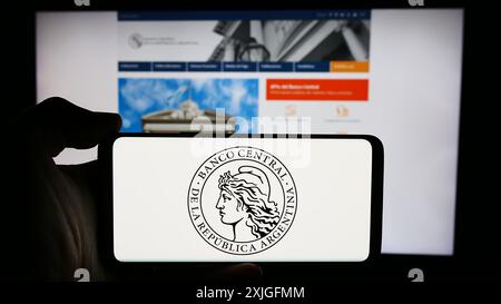 Person, die ein Mobiltelefon mit dem Logo der Banco Central de la Republica Argentina (BCRA) vor der Webseite hält. Schwerpunkt auf dem Display des Telefons. Stockfoto