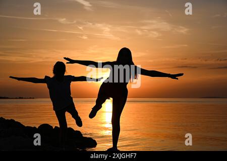 Mutter und Tochter üben Yoga am Strand bei Sonnenuntergang und genießen einen friedlichen Moment zusammen. Stockfoto