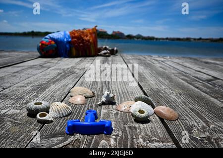 Sommeraccessoires sitzen auf einem hölzernen Dock mit einer Strandtasche im Hintergrund. Stockfoto