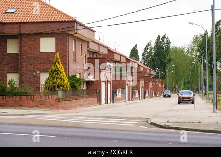 Astorga, Spanien - 3. Juni 2023: Eine Reihe von Ziegelgebäuden mit Garagen und Balkonen in einer ruhigen Straße in Astorga, Spanien, mit einem einzigen Auto, das hinunterfährt Stockfoto