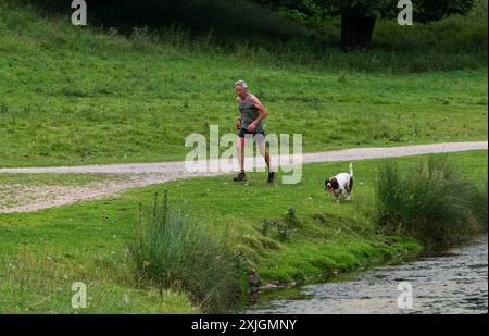 Ripon, North Yorkshire, 18. Juli 2024. Ein Jogger und sein Hund trainieren am frühen Abend im Studley Royal Park nach einem heißen Nachmittag in Nordengland. Stockfoto