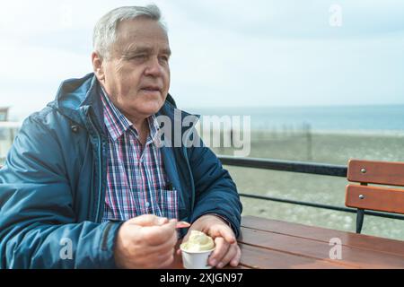 Ein älterer Mann genießt Eis. Ein älterer Herr sitzt allein am Tisch. Stockfoto