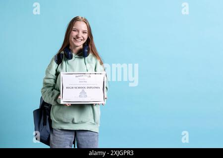 Positives junges Mädchen, das den Schulpreis hält, fühlt sich überglücklich nach dem Abschluss des Diploms. Strahlende Frau, die lächelt, nachdem sie Ehre erhalten hat, positive Emotionen hat, Studiohintergrund Stockfoto