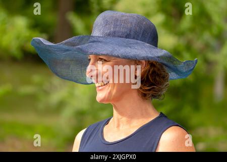 Eine ältere Frau mit blauem Hut, die vor dem Hintergrund der Natur lächelt. Stockfoto