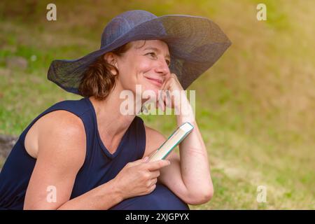 Porträt einer romantischen älteren Frau im Alter von 50-55 Jahren mit blauem Damenhut und einem Buch. Stockfoto