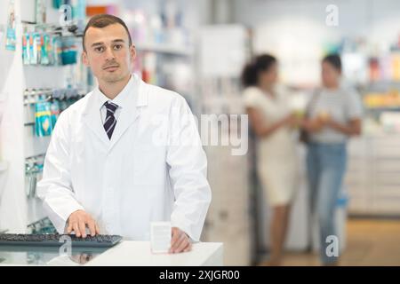 Junger männlicher Apotheker, der am Schreibtisch mit der Tastatur in der Apotheke steht Stockfoto