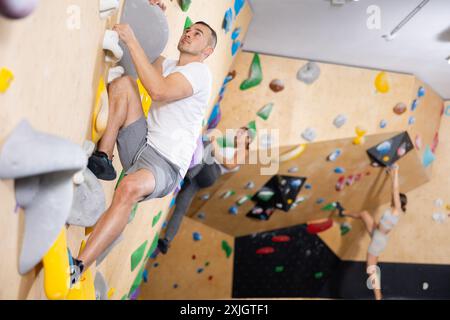 Fokussierter Mann, der die Boulderwand in der Kletterhalle aufsteigt Stockfoto