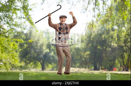 Ein älterer Mann, der einen Gehstock hält und draußen in der Natur einen Hula Hoop dreht Stockfoto