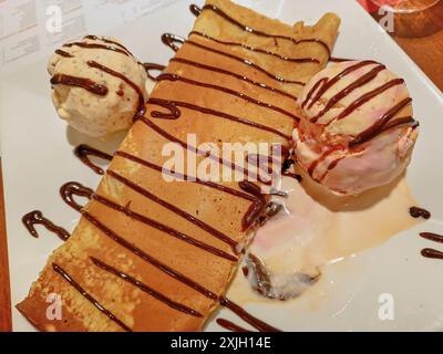 Pfannkuchen gefüllt mit Blancmange, begleitet von Lucuma, Vanille und Erdbeereis dekoriert mit Schokoladenfudge Stockfoto