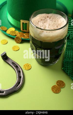 Tasse dunkles Bier mit Kobold Hut, Hufeisen und Münzen auf grünem Hintergrund. St. Patrick's Day Stockfoto