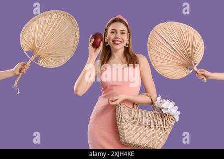 Schöne junge Frau, die süße Mangobrüchte und Hände mit getrockneten Palmblättern auf Fliederhintergrund hält Stockfoto