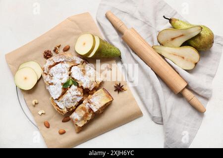 Stücke leckerer Birnenstrudel mit frischen Früchten und rollendem Pin auf beigem Hintergrund Stockfoto