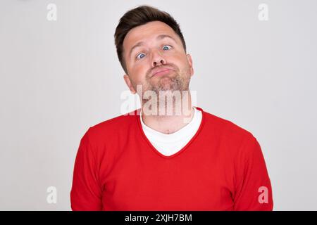 Verwirrter Kerl mit rotem T-Shirt, der mit Zweifeln in die Kamera schaut. Stockfoto