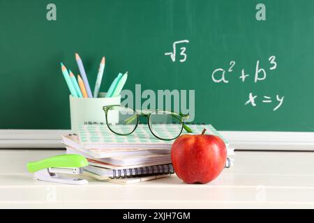 Apfel, Brillen und Schreibwaren auf dem Schreibtisch in der Nähe der Tafel mit Formeln. Back-to-School-Konzept Stockfoto