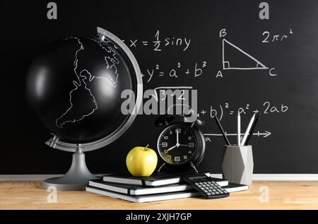 Apfel, Globus, Wecker und Schreibwaren auf dem Schreibtisch in der Nähe der Tafel mit Formeln. Back-to-School-Konzept Stockfoto