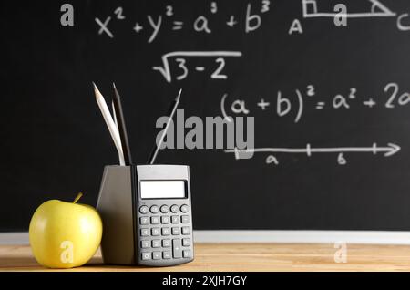 Apfel, Taschenrechner und Bleistifte auf dem Schreibtisch in der Nähe der Tafel mit Formeln. Back-to-School-Konzept Stockfoto