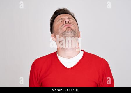 Verwirrter Kerl mit rotem T-Shirt, der mit Zweifeln in die Kamera schaut. Stockfoto