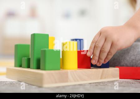 Kleines Mädchen, das mit geometrischen Holzfiguren auf dem Teppich spielt, Nahaufnahme. Kindergartenaktivitäten zur motorischen Entwicklung Stockfoto