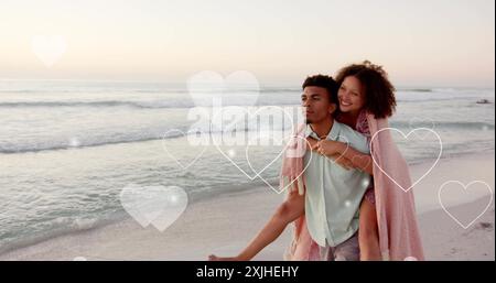 Bild von Herzen, die sich über einen birassischen Mann bewegen, der im Sommer eine Frau mit Huckepack am Strand trägt Stockfoto