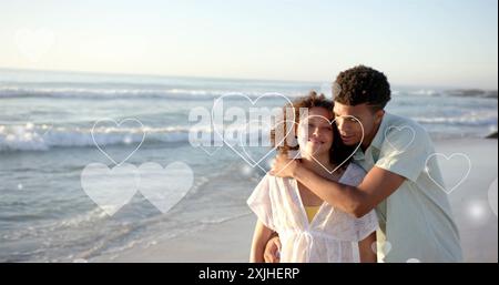 Bild von Herzen, die sich über verschiedene verliebte Paare am Strand im Sommer bewegen Stockfoto