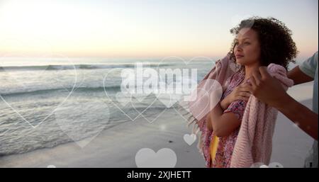 Bild von Herzen, die sich über verschiedene verliebte Paare am Strand im Sommer bewegen Stockfoto