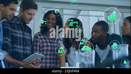 Bild von ökologischen Symbolen über verschiedenen Kollegen, die ein Tablet im Büro verwenden Stockfoto