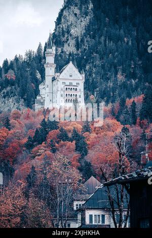 Schloss Neuschwanstein steht hoch in den Bayerischen Alpen, umgeben von einem Wald aus Herbstfarben. Seine weißen Steintürme und Mauern ragen über die Bäume, Stockfoto