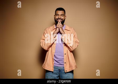 Hübscher afroamerikanischer Mann in modischer Kleidung posiert vor einer leuchtend braunen Wand. Stockfoto