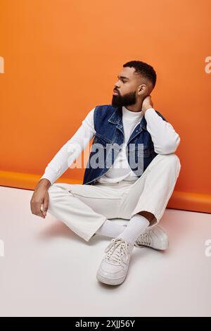 Hübscher afroamerikanischer Mann, der in trendigem Outfit vor lebendigem Hintergrund sitzt. Stockfoto